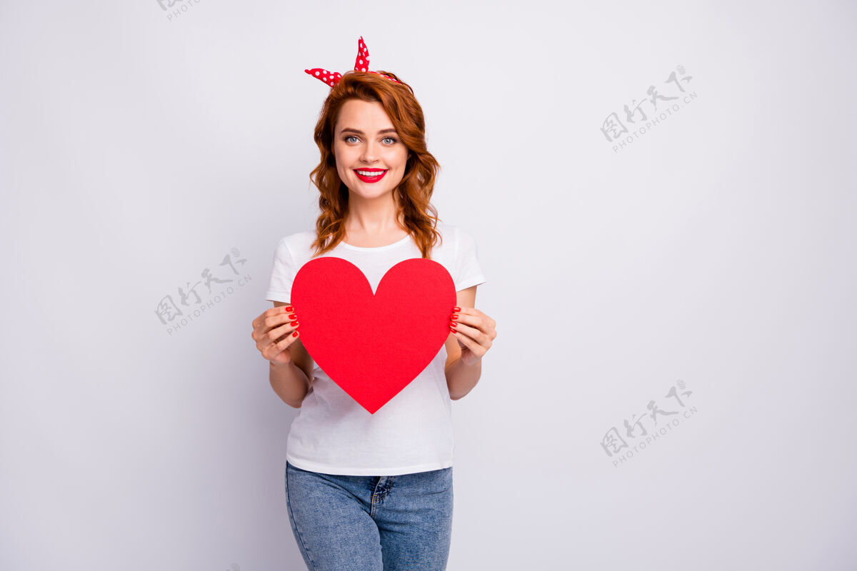 大可爱可爱女孩的肖像手持大纸卡心形她在2月14日庆祝日穿上好看的衣服隔着白色的墙年轻日期感情