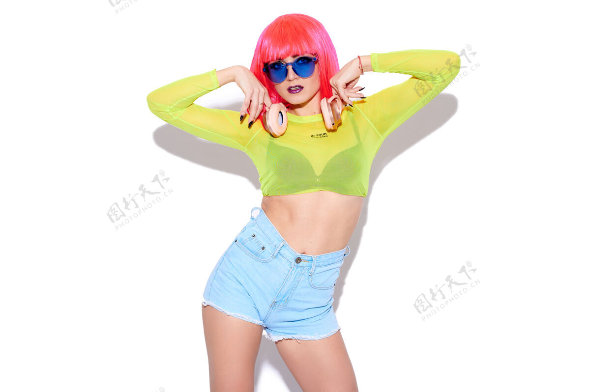 艺术性感的时髦女孩dj穿着色彩鲜艳的衣服 粉色的假发和白色背景的耳机音乐多彩配件