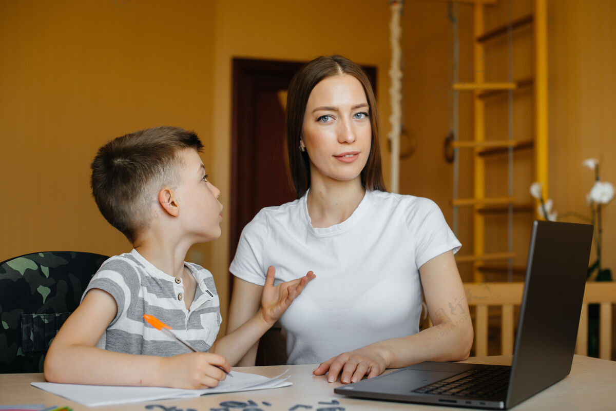 支持一位母亲和她的孩子在家里电脑前从事远程教育呆在家里 训练写作语言控制