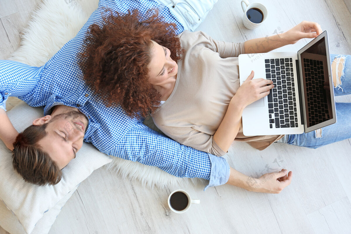 枕头家里有笔记本电脑的快乐年轻夫妇购物咖啡地毯