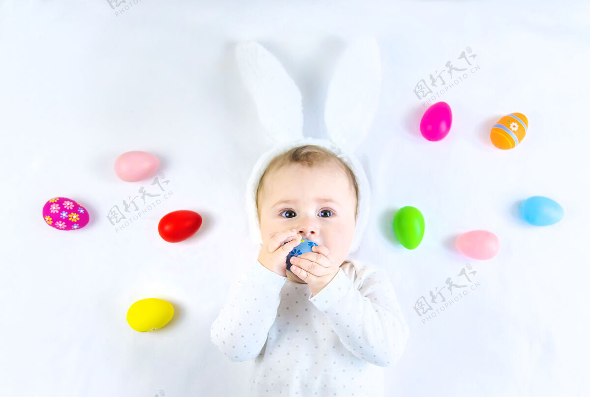 欢呼宝宝穿得像兔子 在白色的表面上放复活节彩蛋童年微笑手