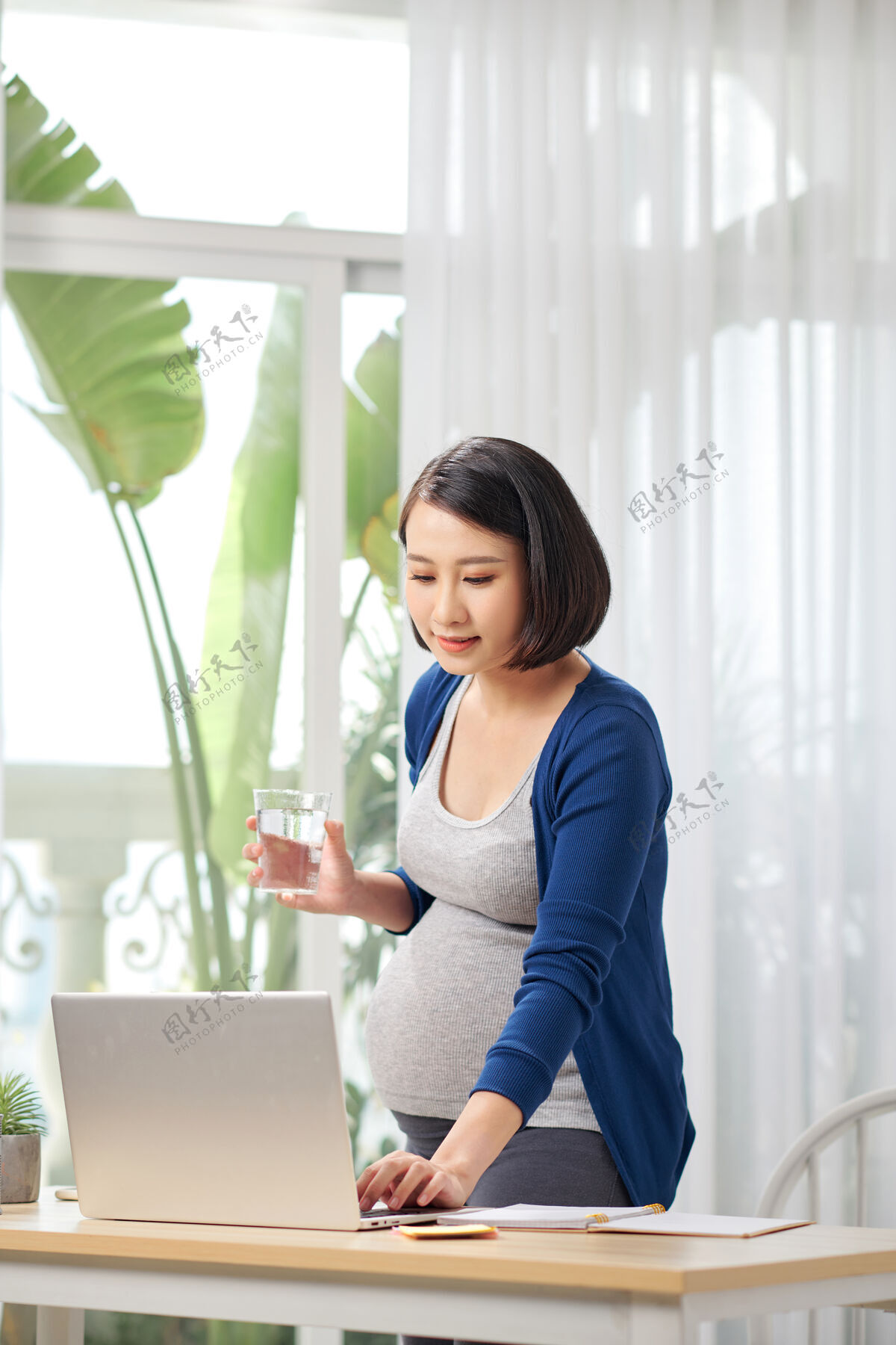 电脑孕妇在家办公桌旁拿着电脑和饮用水房子无线女孩