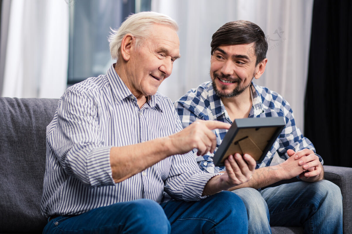 室内兴高采烈的老人和儿子坐在沙发上 手里拿着相框特写保险孙子