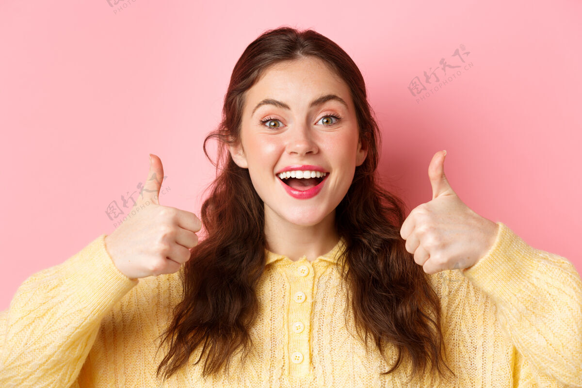 休闲可爱快乐的女人表示支持的特写镜头 竖起大拇指表示赞同 说是的 点头同意 站在粉色的墙上复制空间咧嘴笑年轻候选人