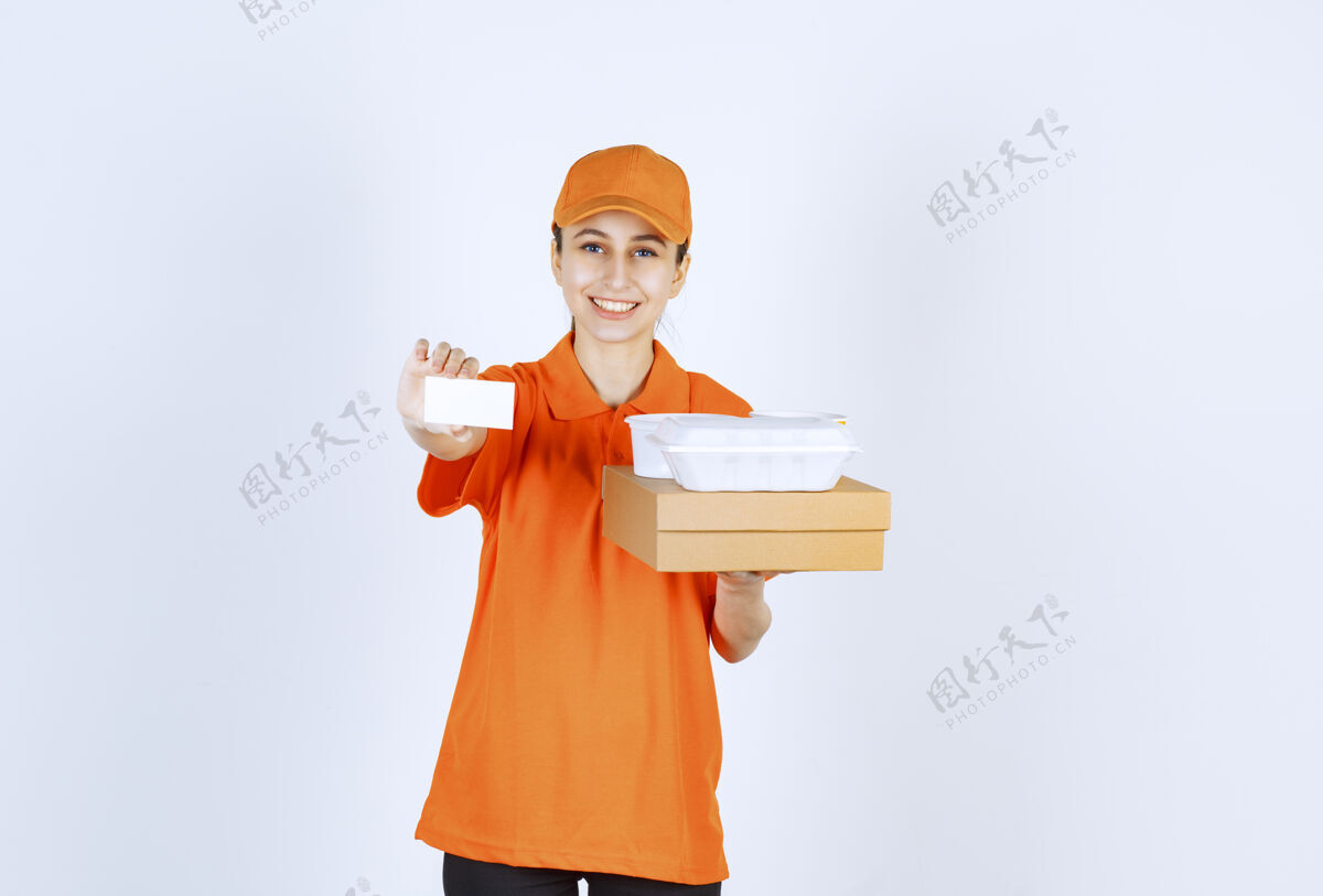 促销身着橙色制服的女快递员在出示名片时 手里拿着一个纸板箱和一个塑料外卖箱休闲姿势预订