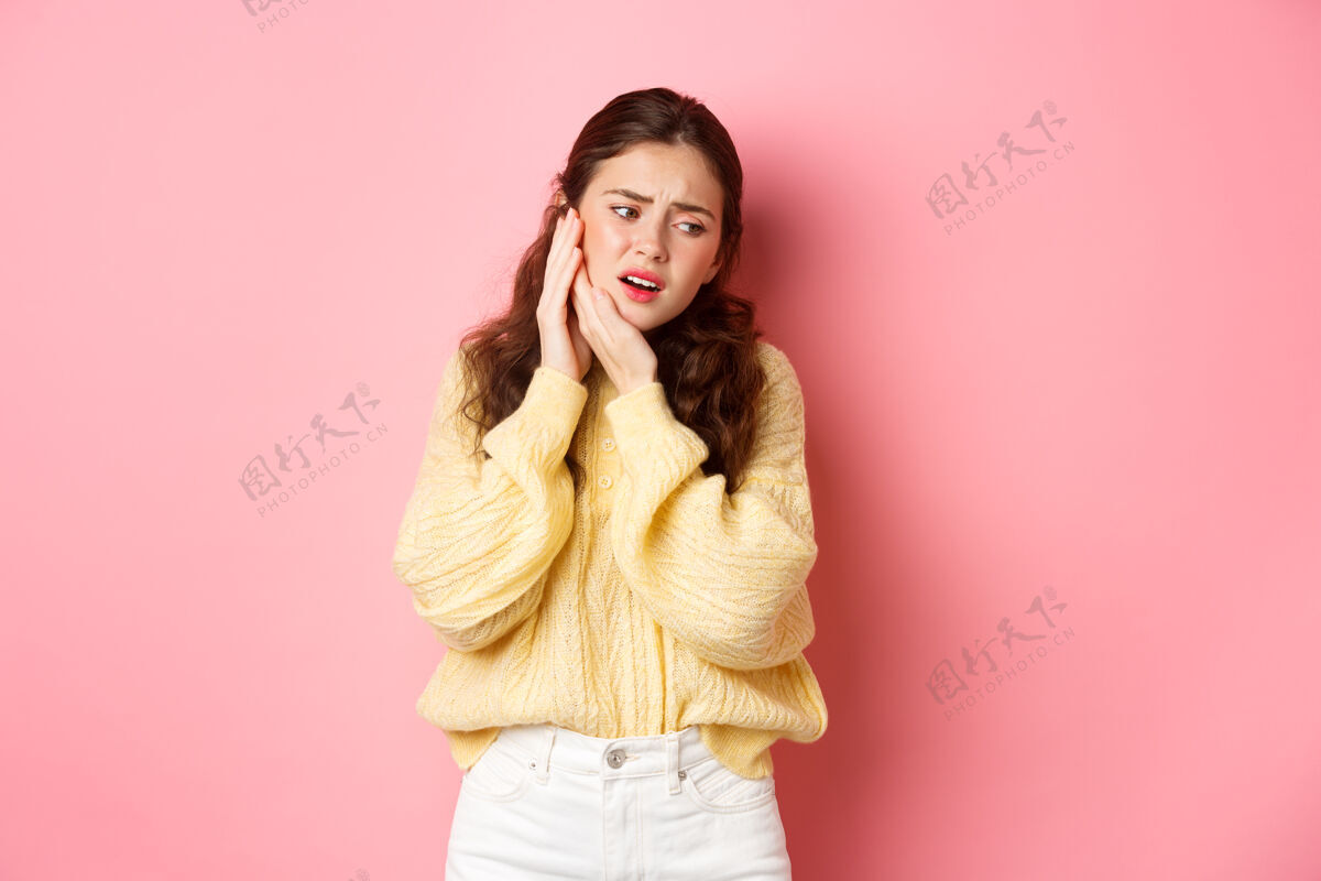 休闲有牙痛的年轻女子 摸着斯瓦伦的脸颊 痛苦地做鬼脸 需要看牙医 口腔科预约 靠着粉红色的墙站着女性情感候选人
