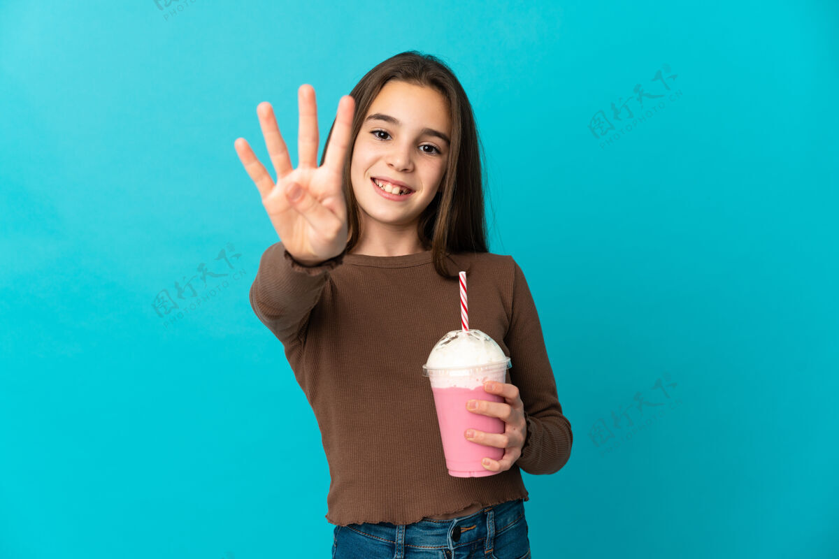 孩子小女孩拿着草莓奶昔孤立在蓝色的墙上快乐地用手指数着四个玻璃可爱刷新