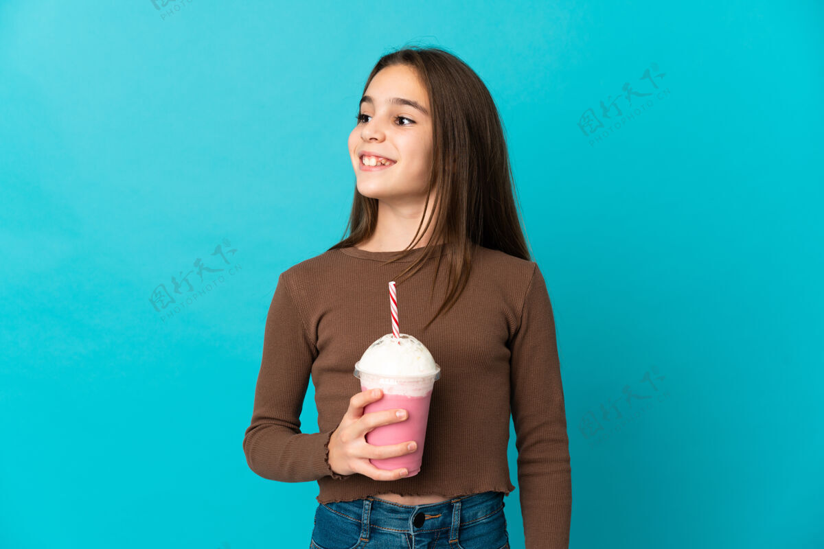 孩子拿着草莓奶昔的小女孩孤零零地站在蓝色的墙上 一边抬头一边想着一个主意年轻有机想象