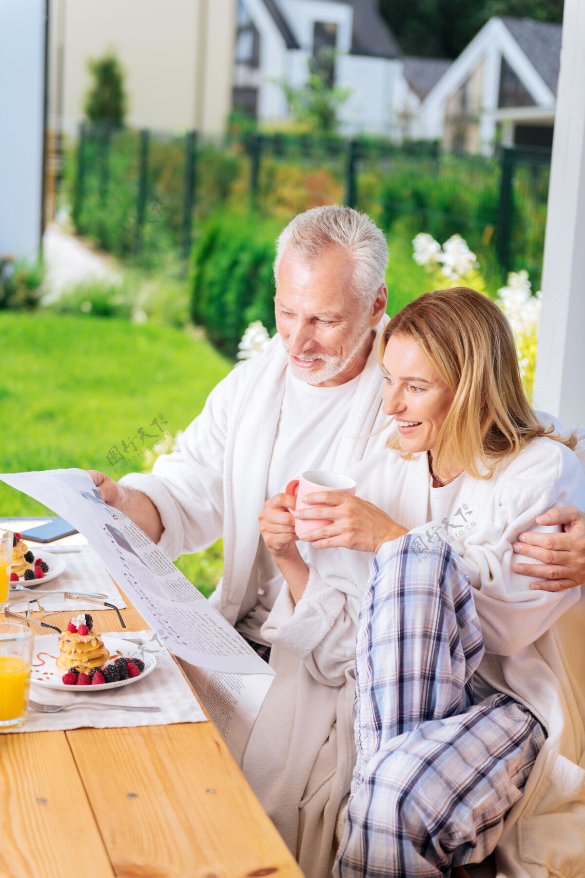 关系靠近丈夫的女人穿着方格睡裤和白色浴衣坐在丈夫旁边的迷人成熟女人放松露台早餐