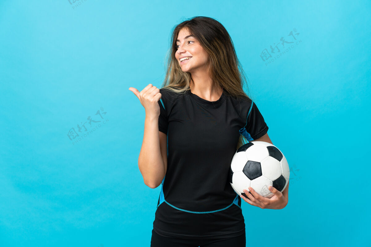 侧线年轻的足球运动员女子孤零零地站在蓝色的墙上 指着旁边的产品赠送手势年轻人信心