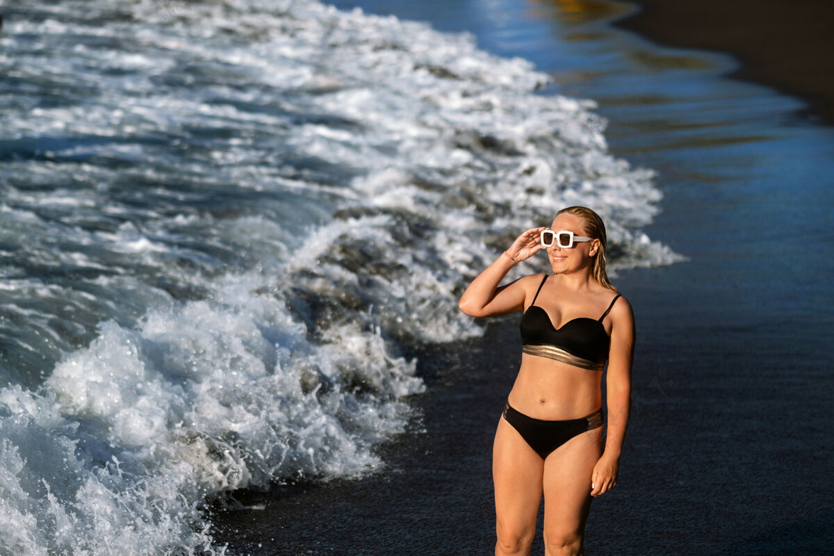 海岸一个穿着黑色泳衣的女孩在沙滩上散步女人比基尼人
