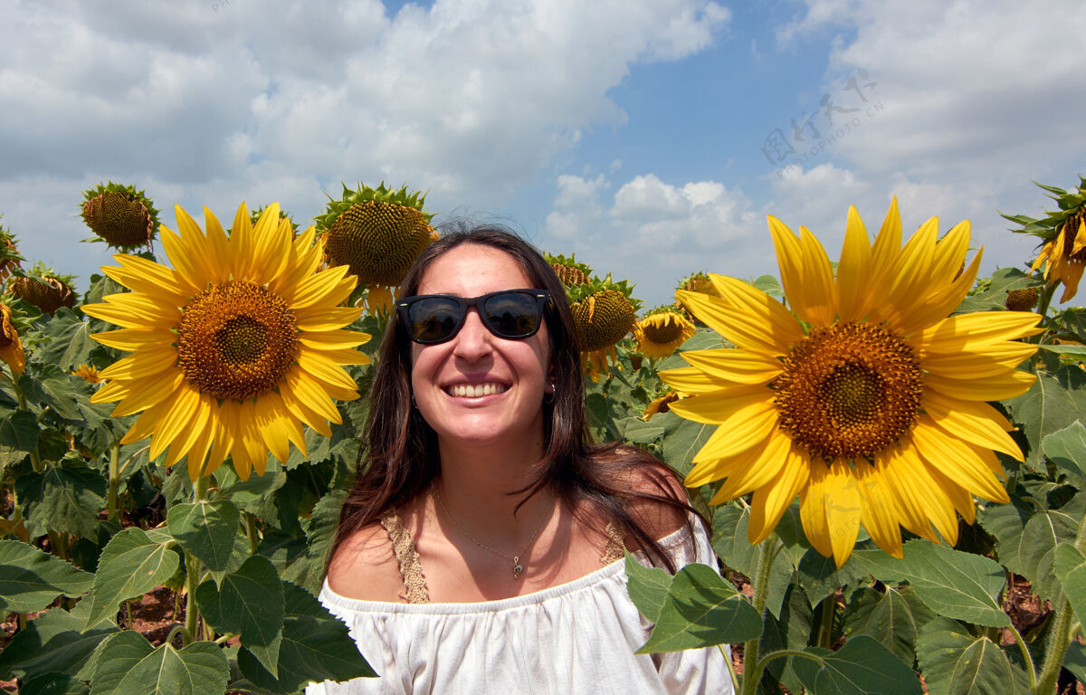 花一个戴着太阳镜的快乐美丽的土耳其女人在向日葵地上摆姿势时尚自然夏天