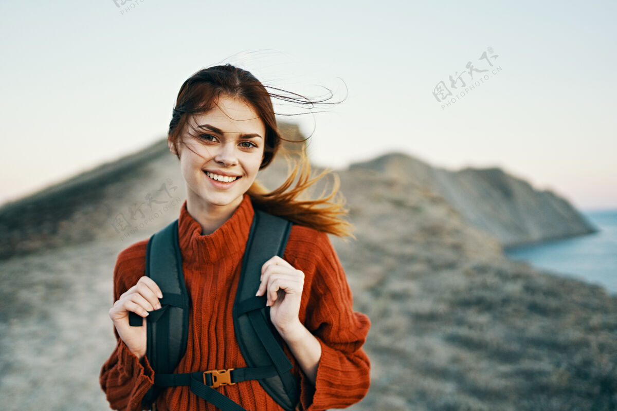 旅游快乐的女人背着背包在大自然的山上靠近大海和夕阳快乐的微笑模式休闲活动年轻人摄影