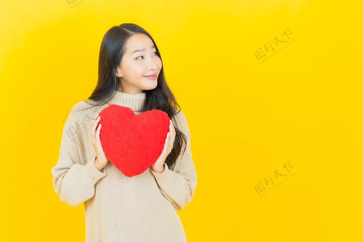 年轻画像美丽的亚洲年轻女子在黄色的墙上以心形枕头微笑华丽时尚女人