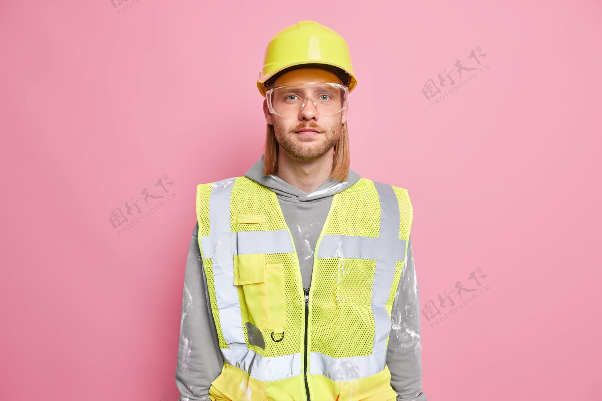 建筑师认真的建筑工人工程师戴施工安全帽制服眼镜看起来自信地准备工作隔离在粉红色的墙壁上自信的工人或建筑工人建筑工人头盔硬地
