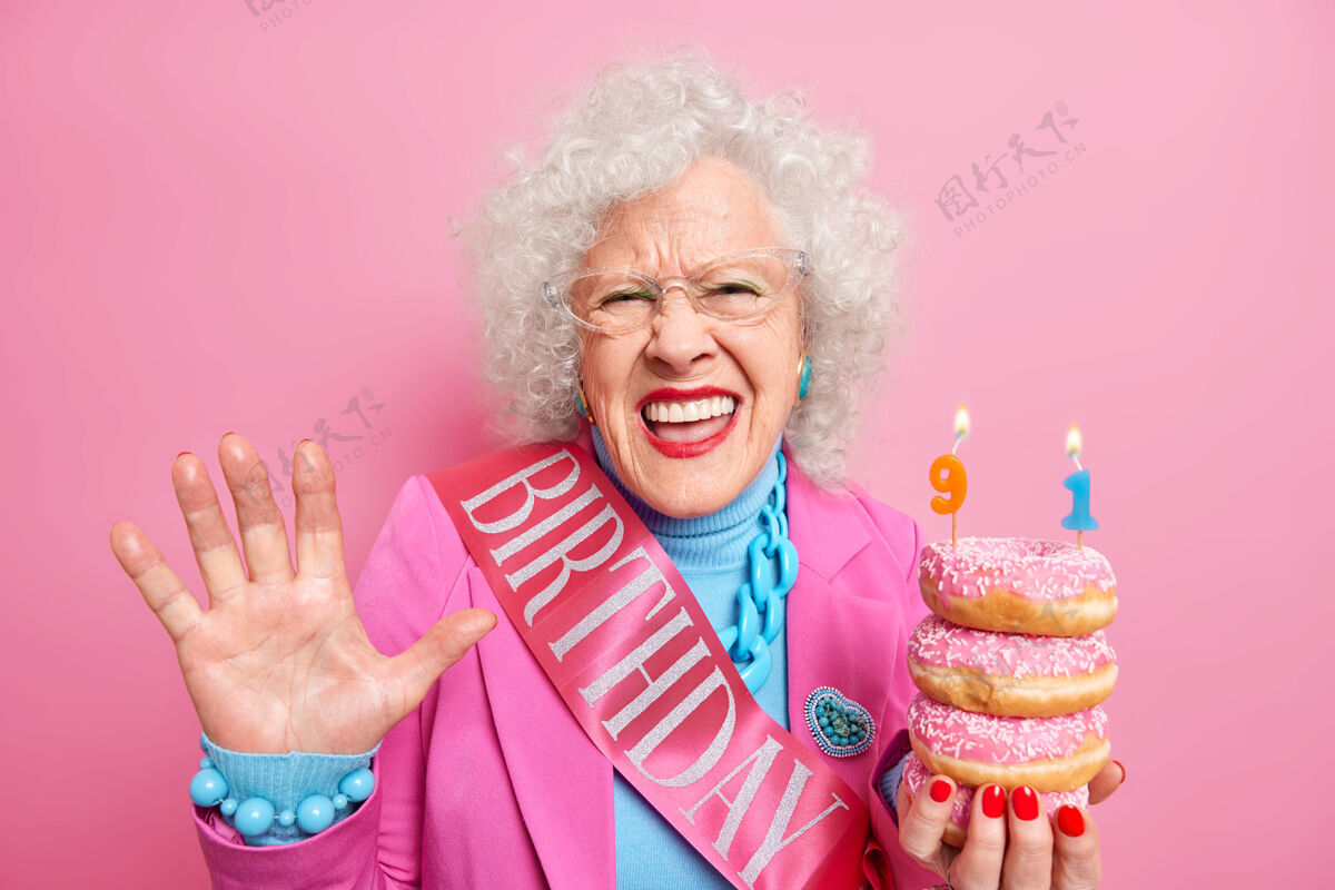 人正卷发女退休老人举着手心感到很高兴捧着一堆油炸圈饼庆祝91岁生日穿上喜庆的衣服女士乐观祖母