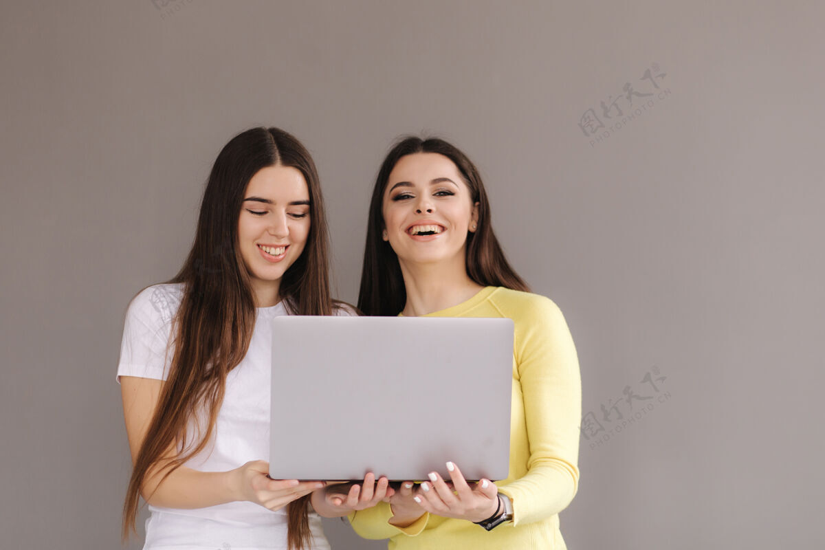 人两个女人抱一个laptop.woman惊讶的看着笔记本电脑微笑毛衣黑发