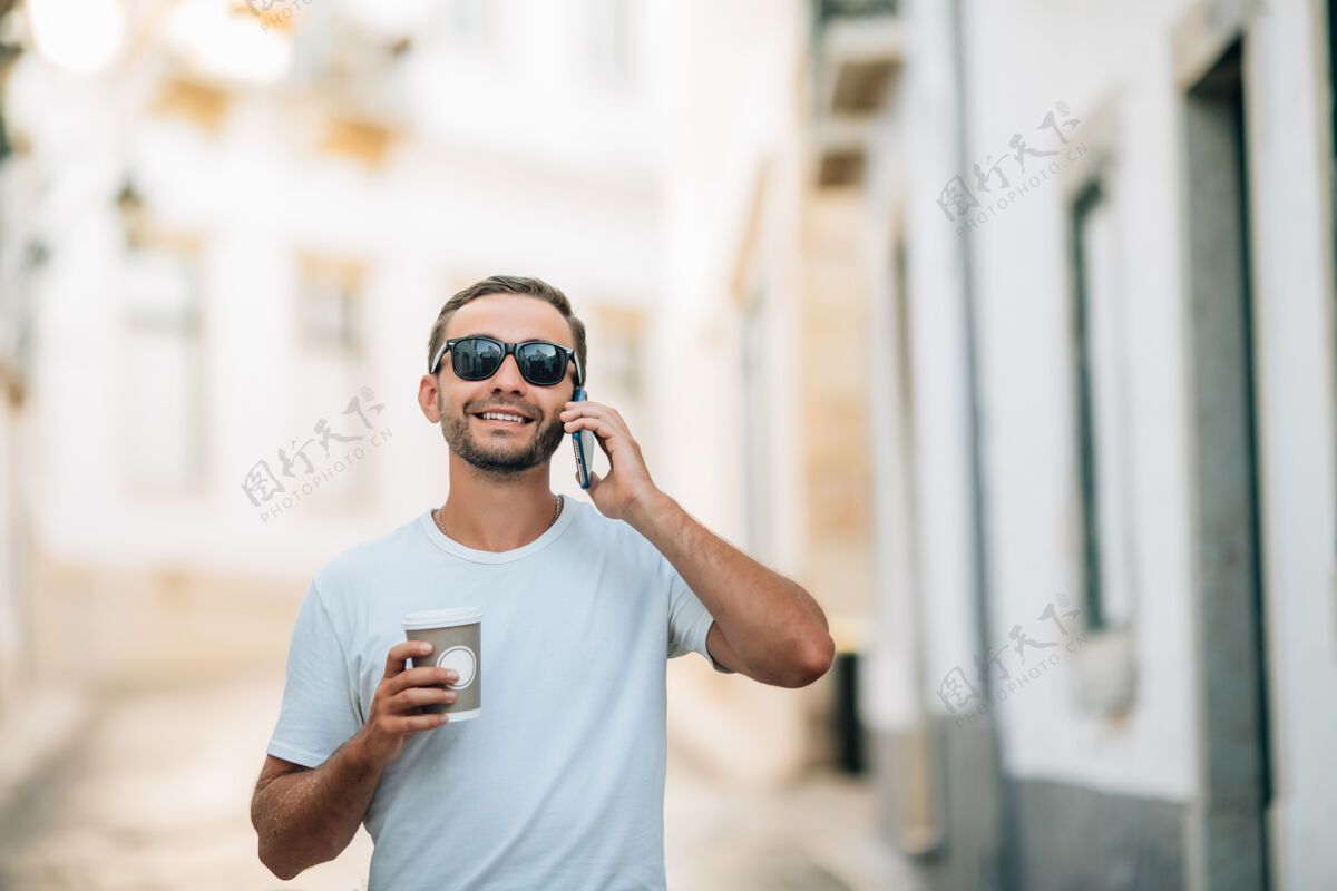 手机穿着时髦服装的帅哥在城市街上打电话通话人散步