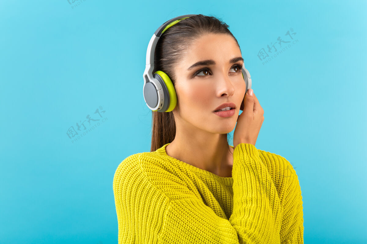 无线迷人时尚的年轻女子戴着无线耳机听音乐快乐地穿着黄色针织毛衣五颜六色的时尚造型摆姿势女人音乐女人