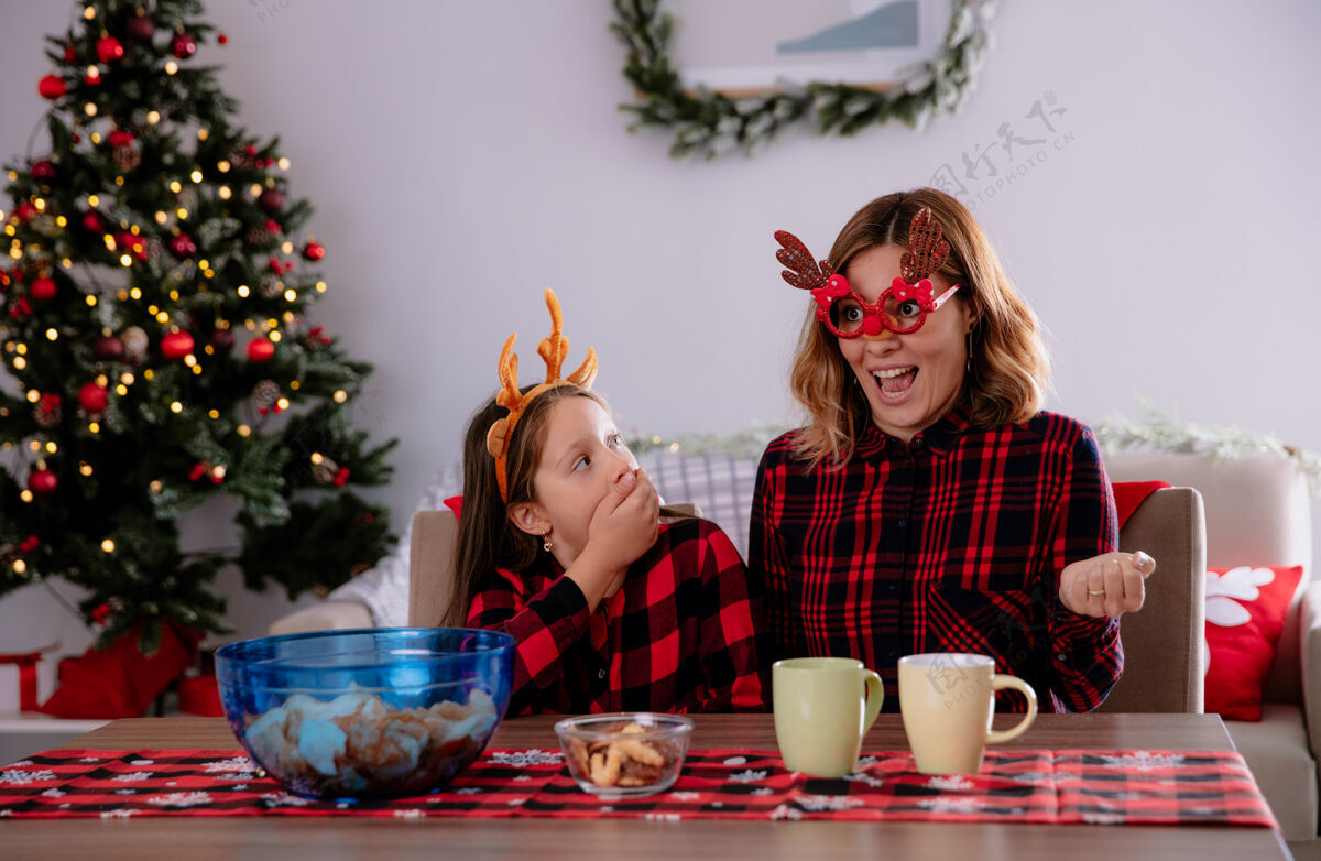 惊喜惊讶的女儿看着坐在餐桌旁的母亲在家里享受圣诞节的时光桌子女儿时间