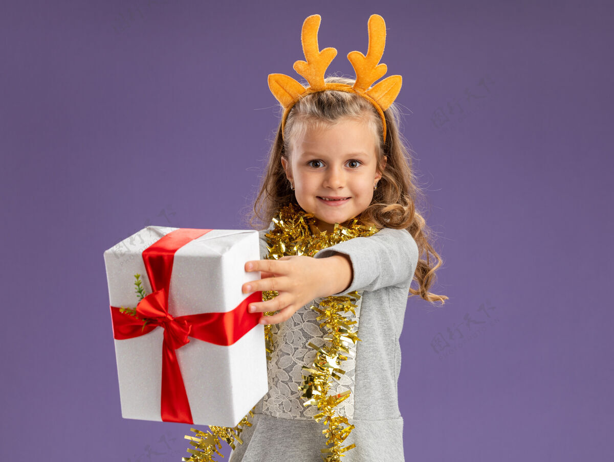 抱微笑的小女孩戴着圣诞发箍 脖子上戴着花环 手里拿着礼品盒 孤零零地贴在蓝色的墙上穿花环脖子