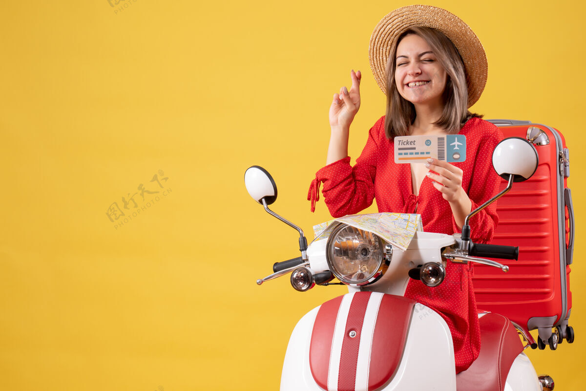 冒险正面图：穿着红裙子的年轻女士手持轻便摩托车上的订票许愿牌人旅游红色