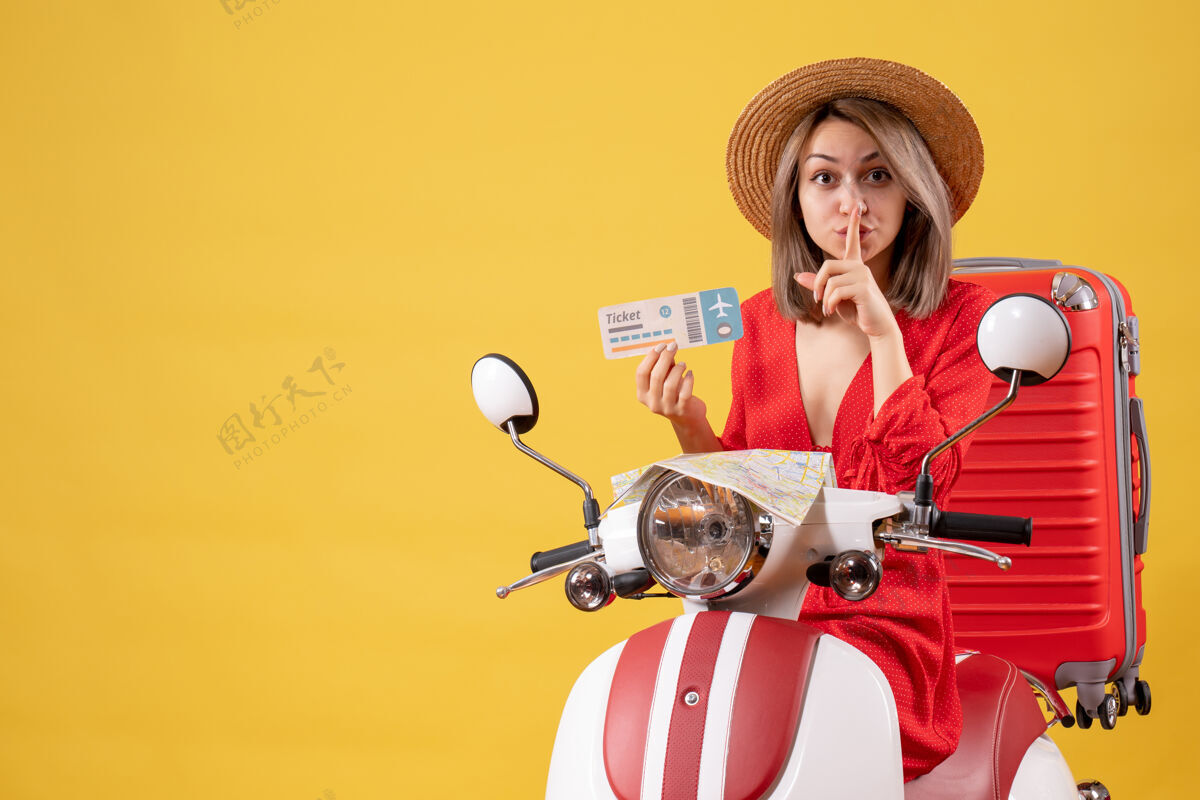 旅游正面图：身穿红色连衣裙的年轻女士手持在轻便摩托车上制作安静标志的门票冒险旅游人