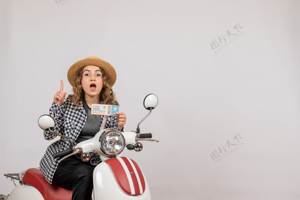指向前视图：坐在轻便摩托车上的年轻女孩拿着车票 手指朝上票轻便摩托车游客