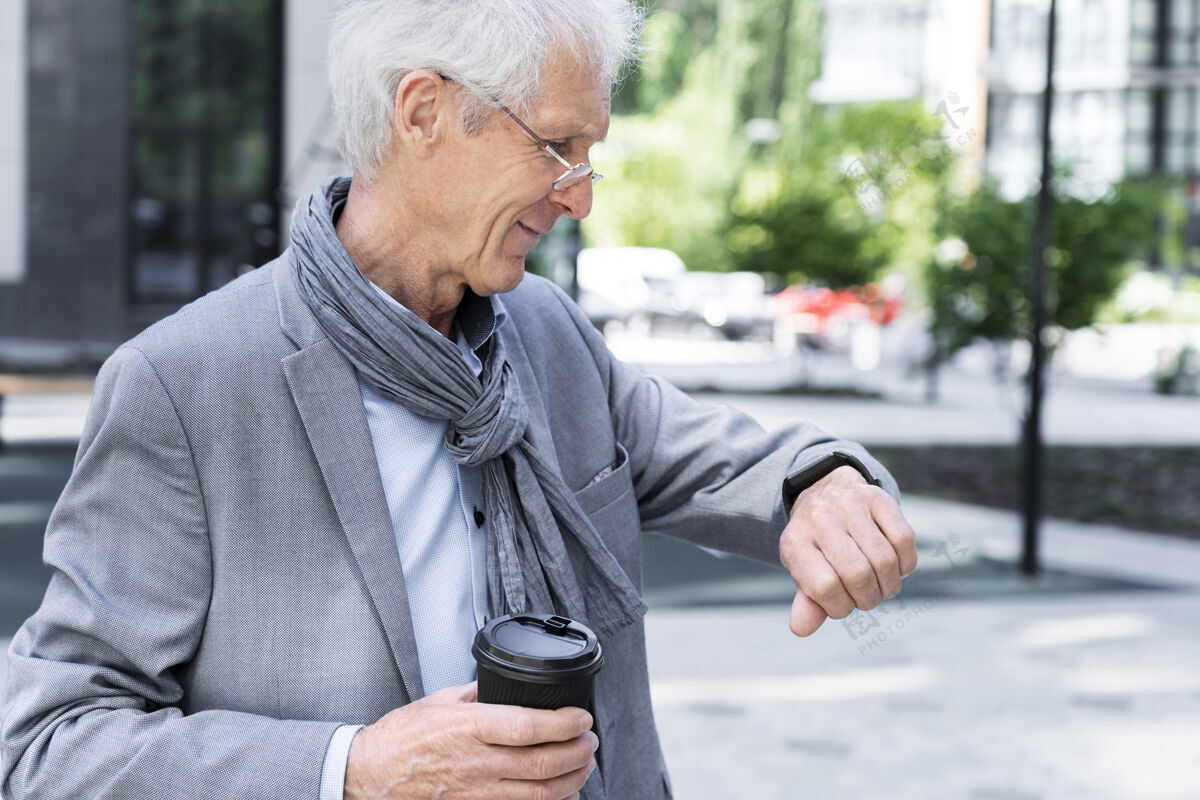 男性时尚的老男人在城里看智能手表城市户外老年人
