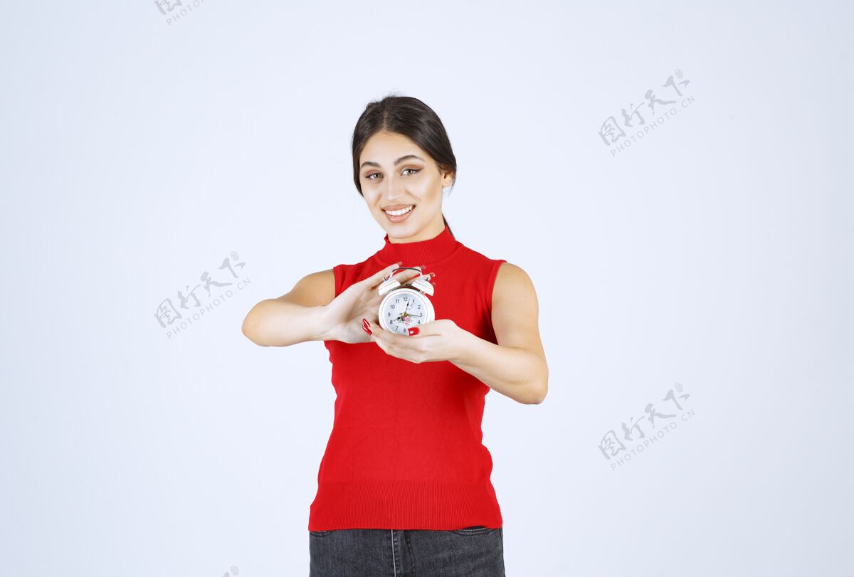年轻人穿红衬衫的女孩拿着闹钟 推销着闹钟工人品牌销售