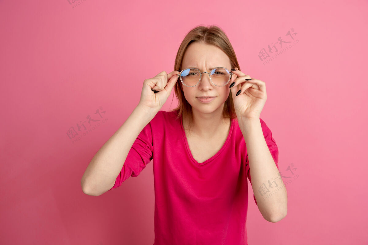 一半戴着眼镜白种人年轻女子的肖像隔离在粉红色的墙上 单色美丽的女模特女孩表达工作