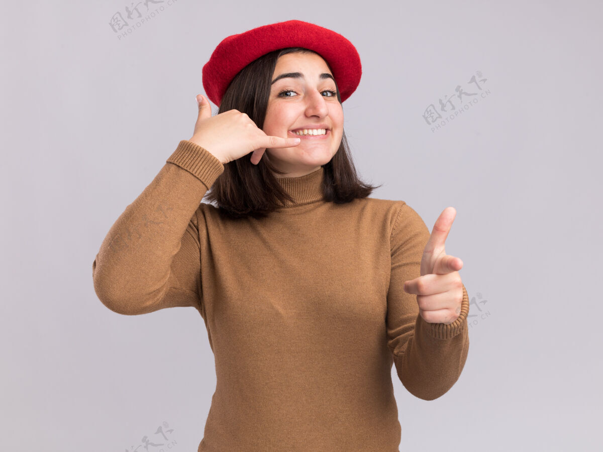 漂亮带着贝雷帽的年轻漂亮白人女孩微笑着 指着摄像机 打着“叫我”的手势手势标志年轻