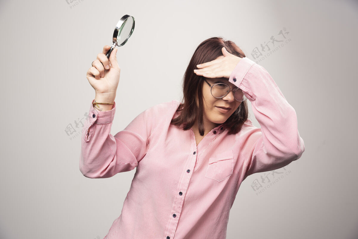 女士穿着粉红色衣服的漂亮女人的肖像 拿着放大镜高质量的照片美女成人手