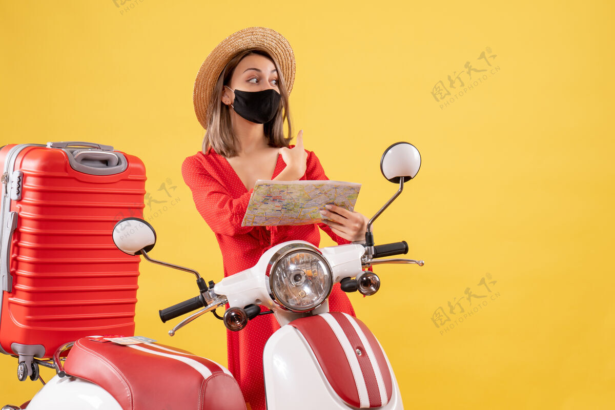 年轻女士正面图戴着黑色面具的年轻女士拿着地图靠近轻便摩托车轻便摩托车旅游滑板车