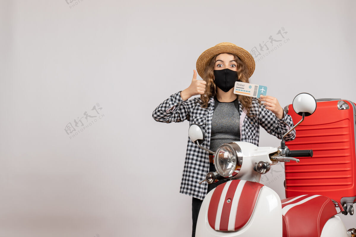 人正面图戴着黑色面具的年轻女孩举着大拇指站在红色轻便摩托车旁边轻便摩托车大拇指持有