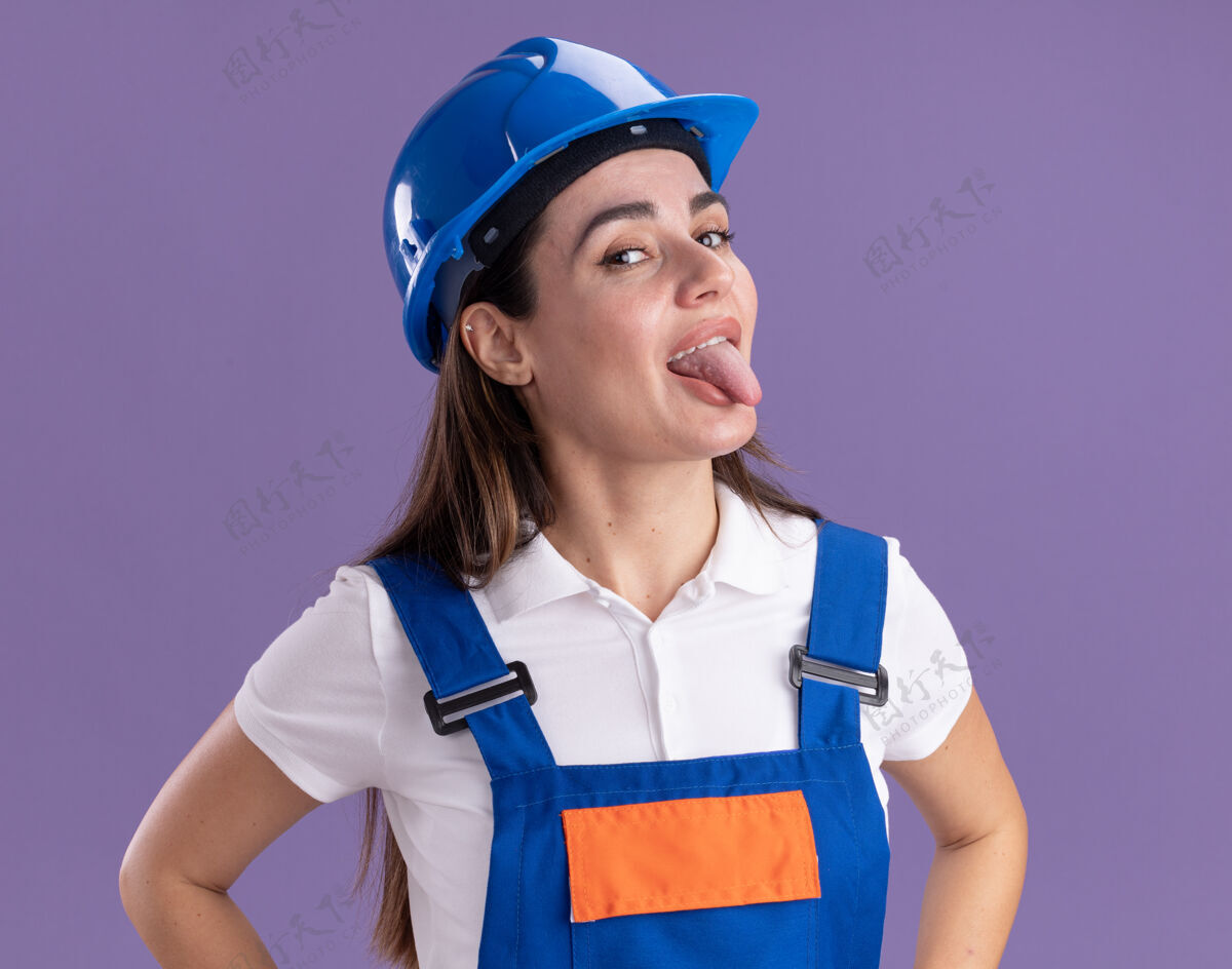 感情穿着制服的年轻建筑工人高兴地在紫色的墙上露出孤立的舌头女人姿势人