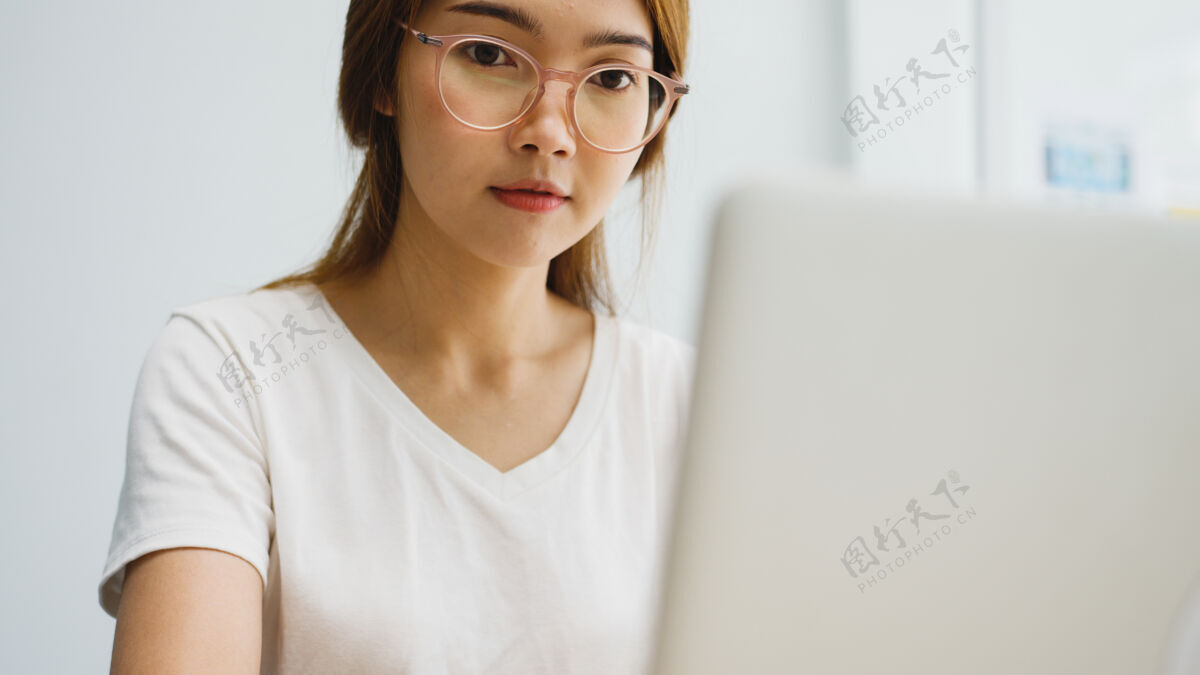 眼镜自由职业的年轻亚洲女商人休闲装使用笔记本电脑在客厅工作在家里办公室在线商务女性