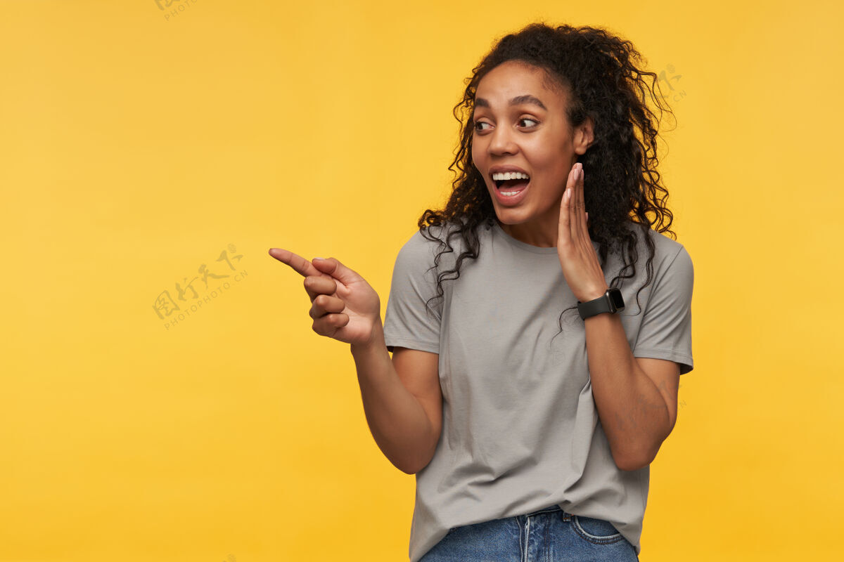 发型年轻的非洲裔美国人穿着灰色t恤 用手指指着旁边的文字空间 脸上洋溢着积极的笑容时尚牛仔女性
