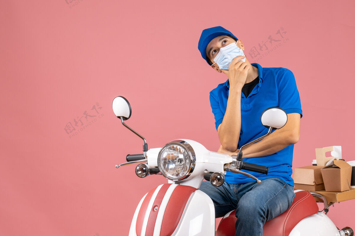 梦幻顶视图梦幻般的送货员戴着医用面罩 戴着帽子坐在粉彩桃色背景的踏板车上滑板车桃技术
