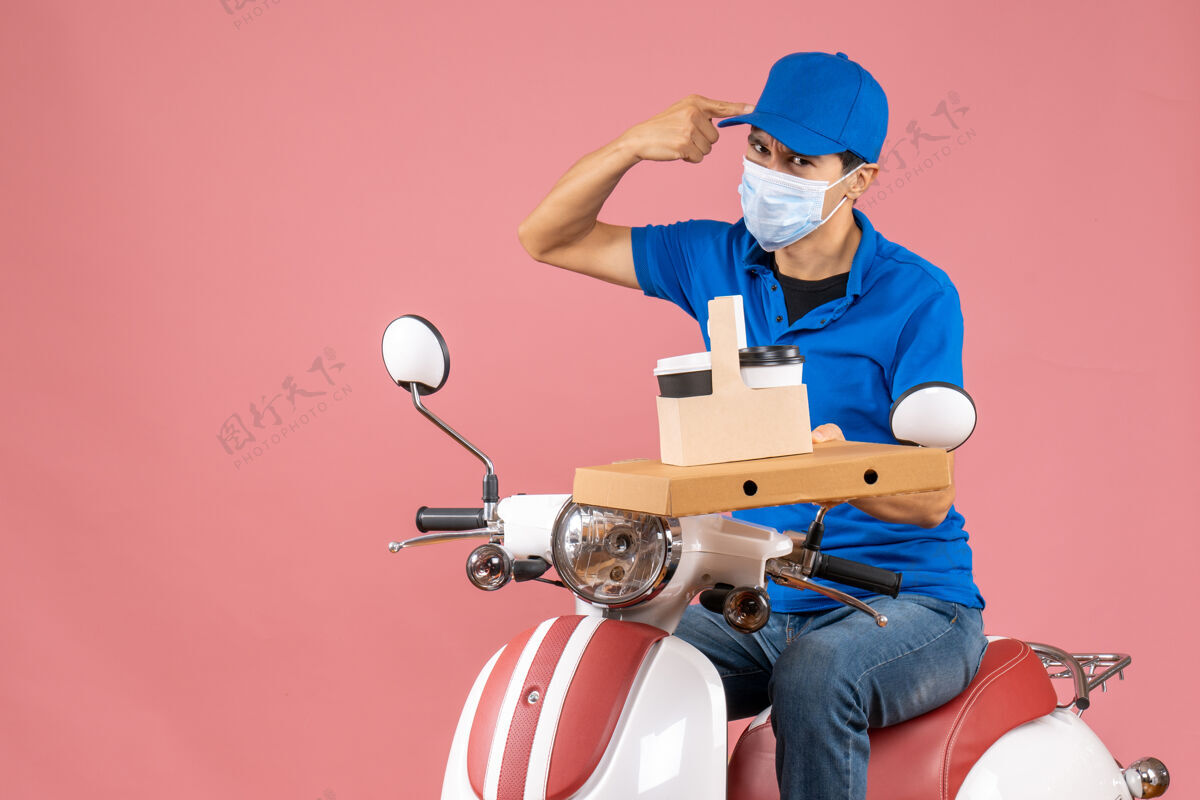 滑板车戴着帽子戴着面具坐在滑板车上的绝望男性送货员的俯视图 在柔和的桃色背景下显示订单桃头盔人物