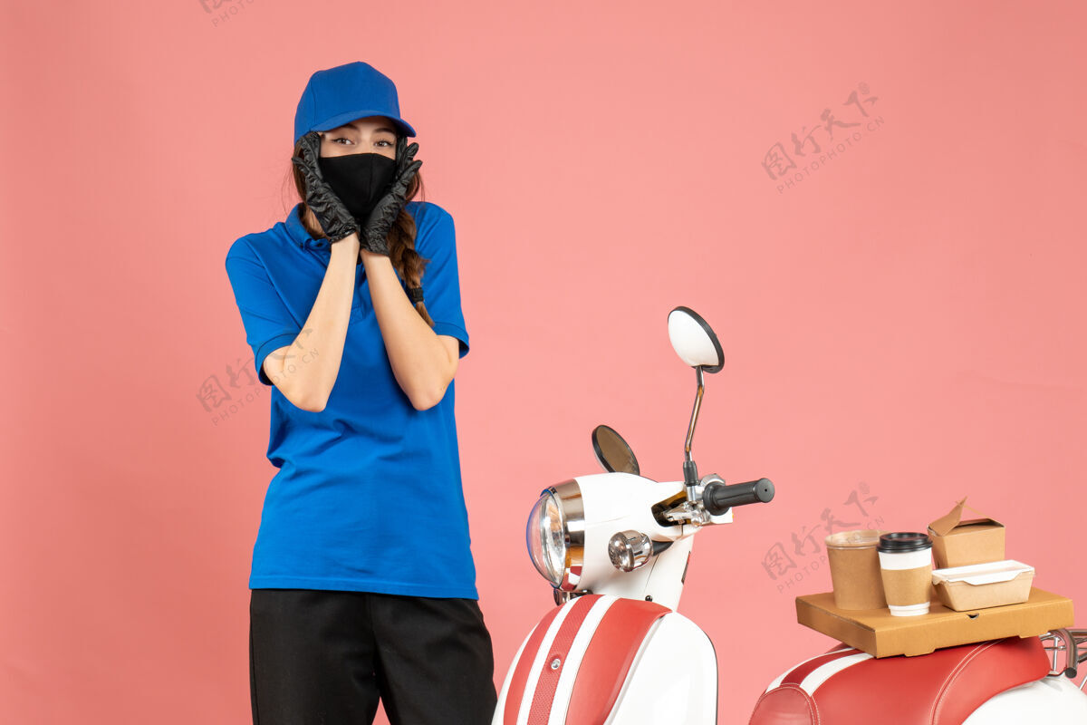 保护套顶视图混乱的快递女孩戴着医用口罩手套站在摩托车旁边 咖啡蛋糕就在粉彩桃色背景上手套困惑人