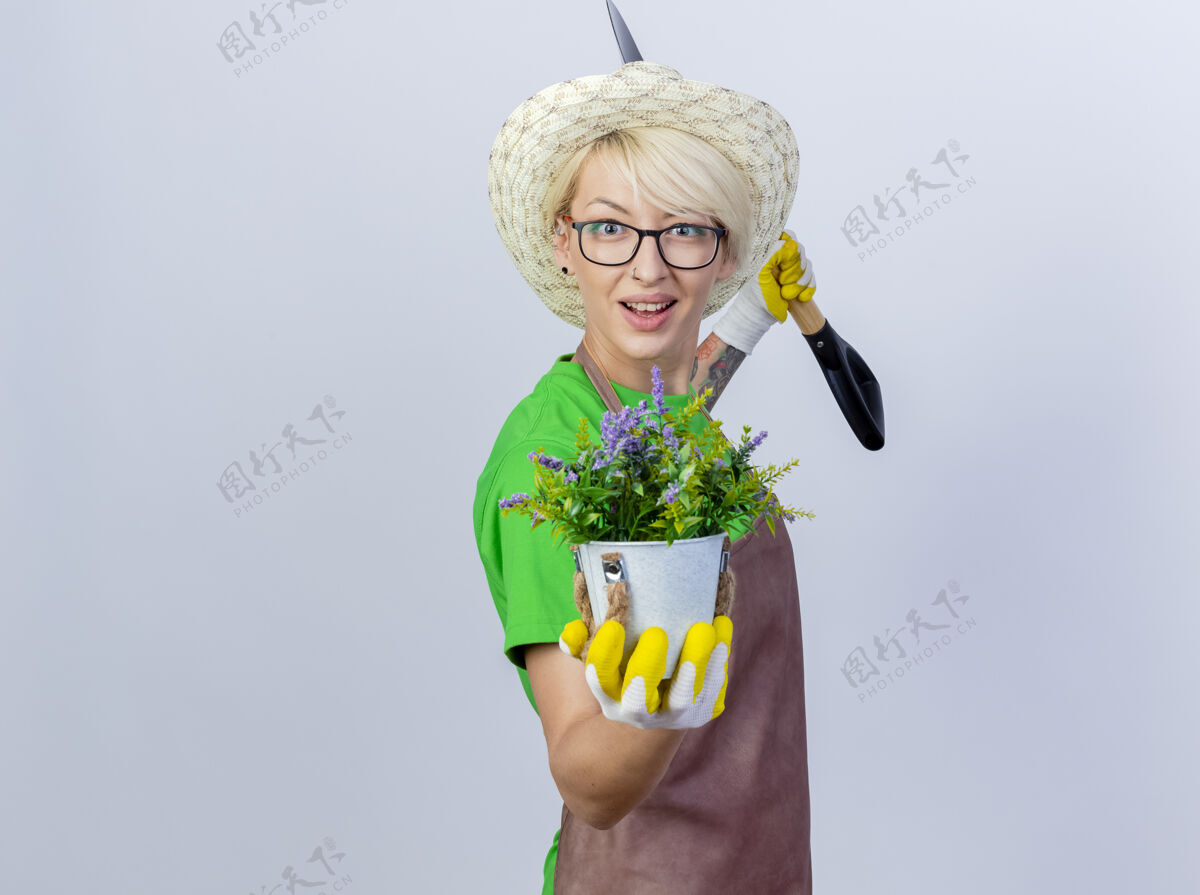 抱一位年轻的园丁 围裙上留着短发 手里拿着铲子 脸上带着微笑 展示着盆栽植物帽子年轻微笑