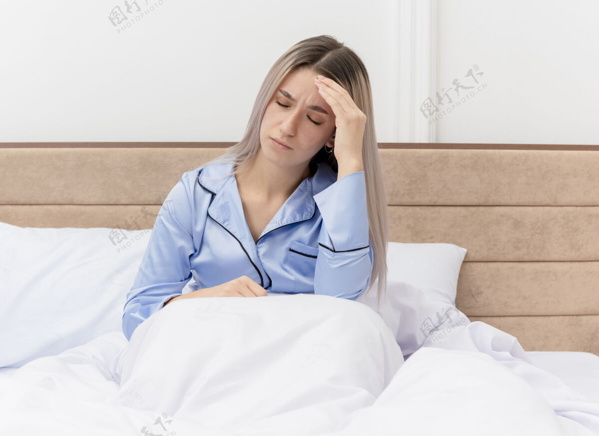 女人穿着蓝色睡衣的年轻漂亮女人坐在床上摸着头 在卧室里头痛头痛床漂亮