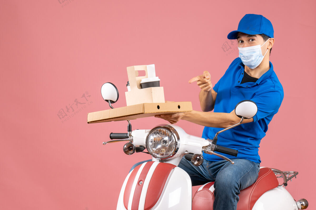 摩托车正面图自信的男性送货员戴着面具戴着帽子坐在滑板车上 在柔和的桃色背景下送货信心背景足球