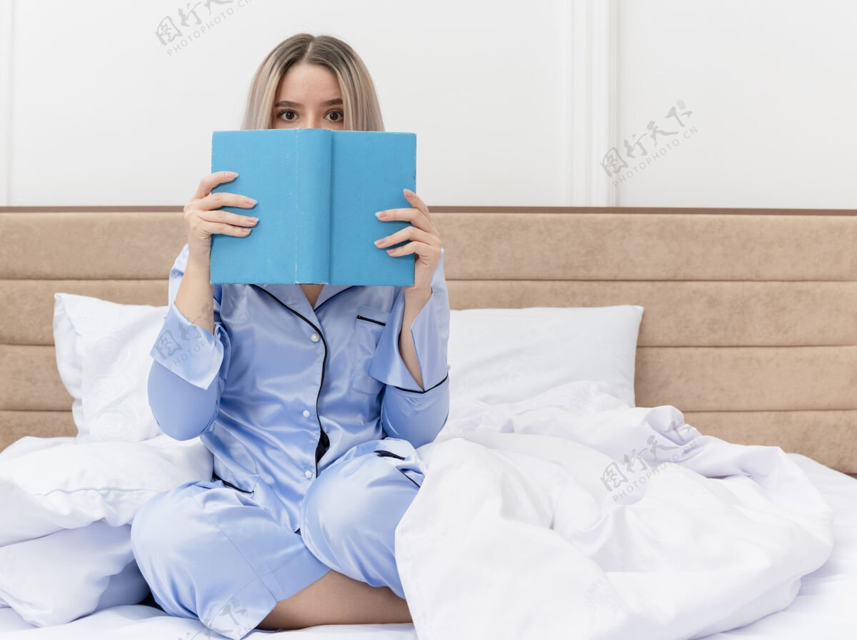 睡衣穿着蓝色睡衣的年轻美女坐在床上 拿着书在卧室里偷看女人偷看床