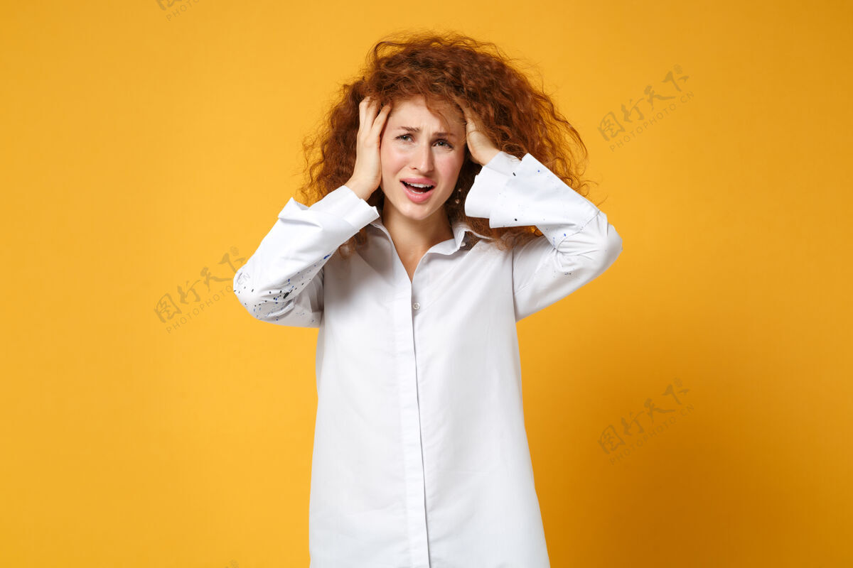 悲伤不满意的心烦意乱的年轻红发女子穿白衬衫的女孩在黄橙色的墙上摆着孤立的姿势人橙色红发