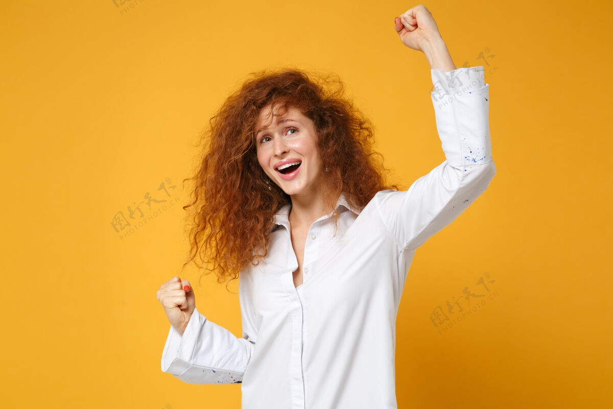 时尚快乐的年轻红发女女孩穿着休闲白衬衫在黄橙色的墙上摆出孤立的姿势脸女士站立