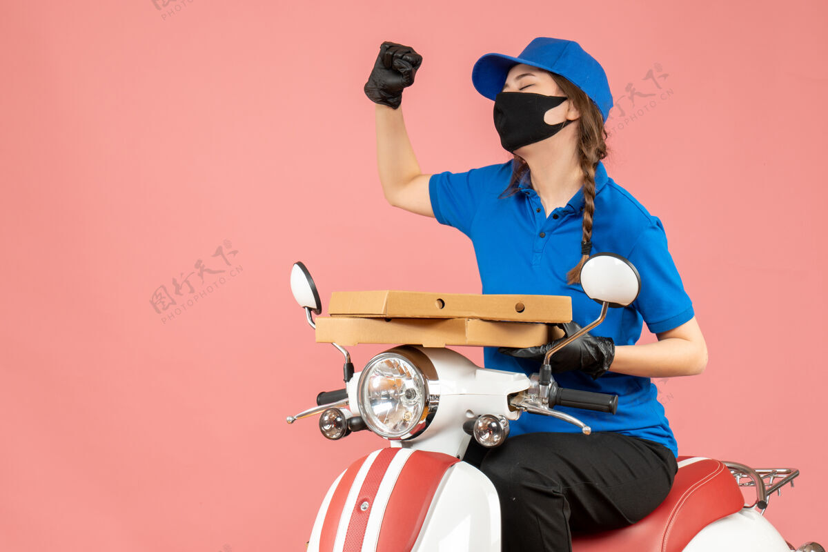 坐着俯视图：年轻快乐的情绪化女快递员戴着医用口罩和手套坐在滑板车上传递粉彩桃的订单情绪桃球员
