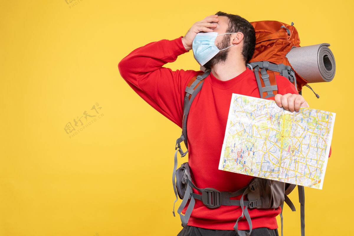 快乐顶视图年轻精疲力竭的旅行者家伙戴着医疗面罩和背包举行黄色地图人人成人