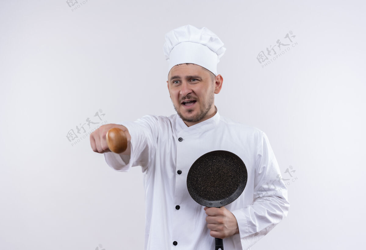 勺子年轻帅气的厨师穿着厨师制服 拿着煎锅 用勺子指着白色的墙壁帅哥拿着指着
